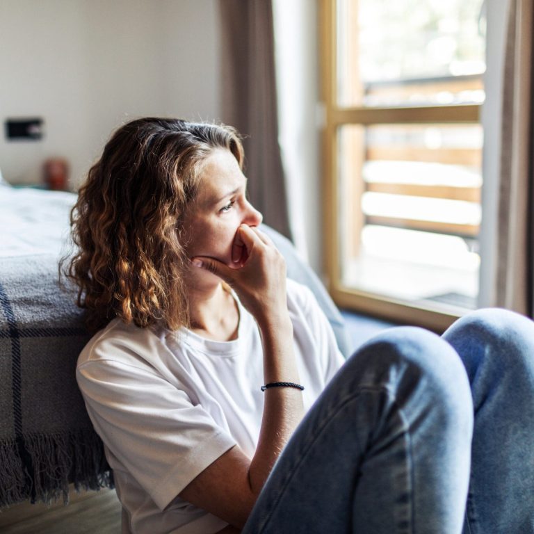 Young adult woman with depression sitting at home alone