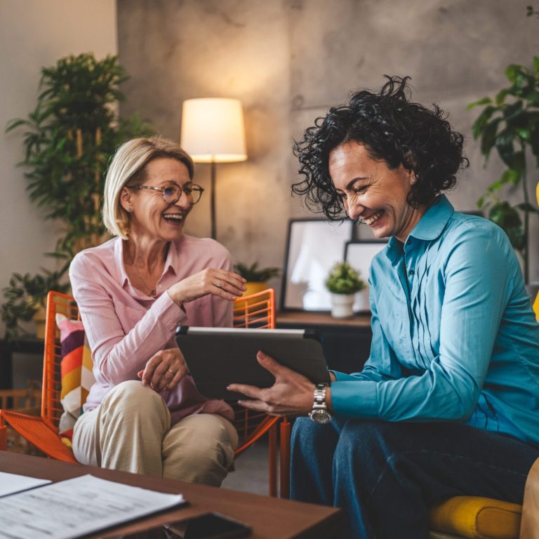 two mature women sit at home hold digital tablet have consultation businesswoman talk about actual tasks and problems
